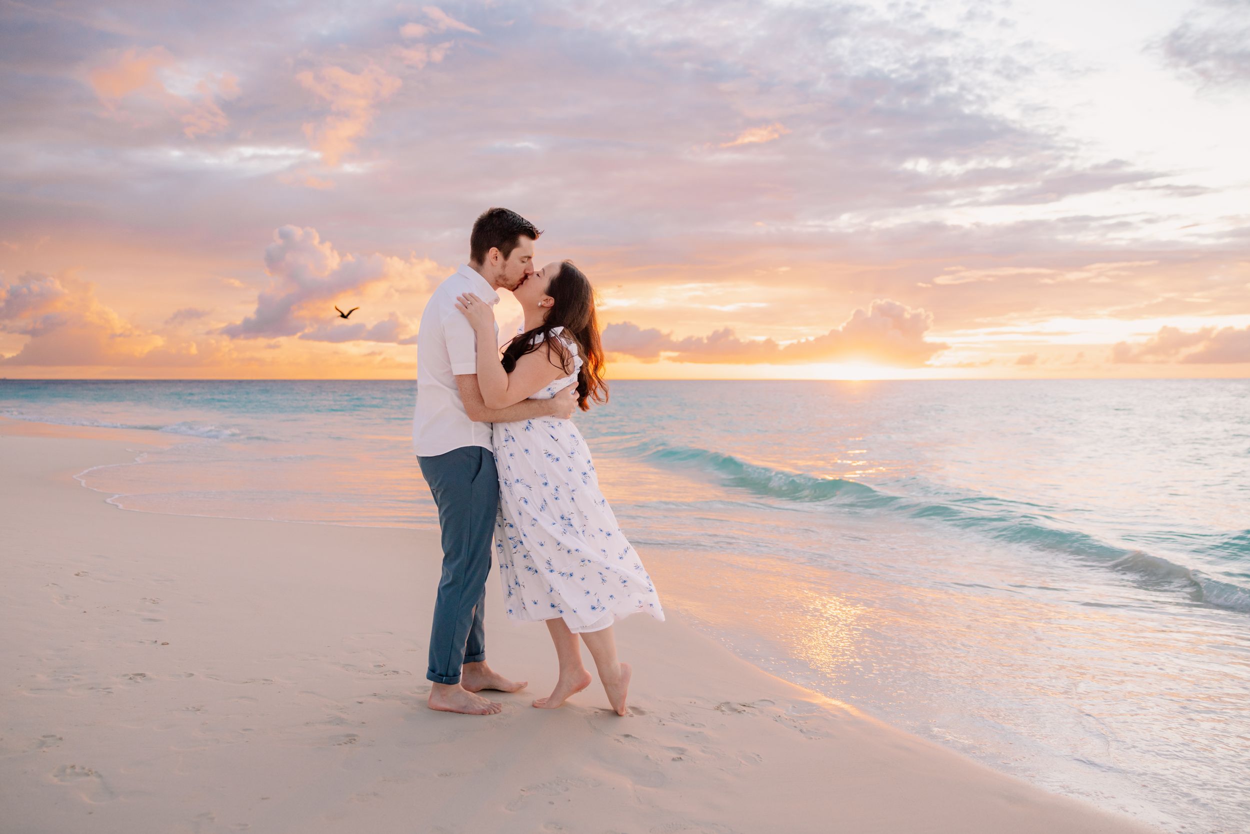 Romantic couple dancing on beach at sunset with orange and pink sky.