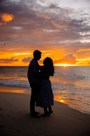 Silhouettes of couple against dramatic orange sunset on beach shore.