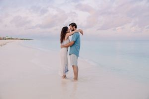Couple sharing tender moments on beach with soft pastel sunset sky.