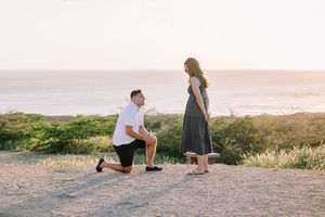 Romantic beach proposal scene at sunset with couple silhouetted against golden sky.