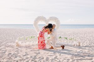 Beach proposal setup with heart shaped flower petals on sand near ocean.