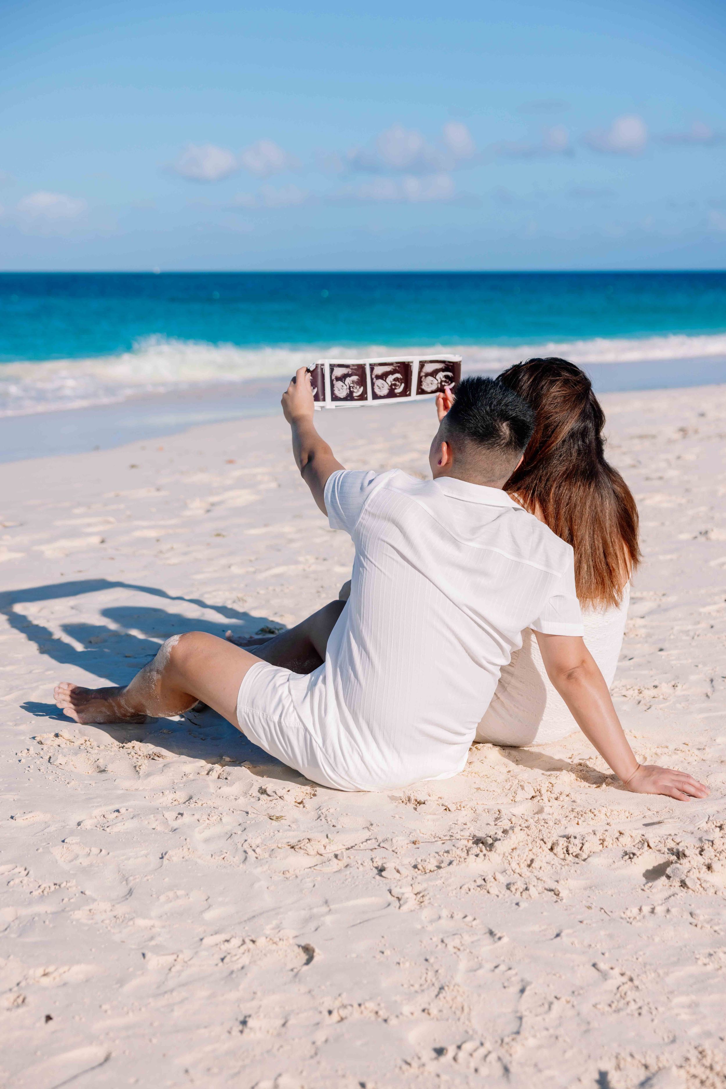 People lying on white sandy beach with crystal blue ocean waters in background.