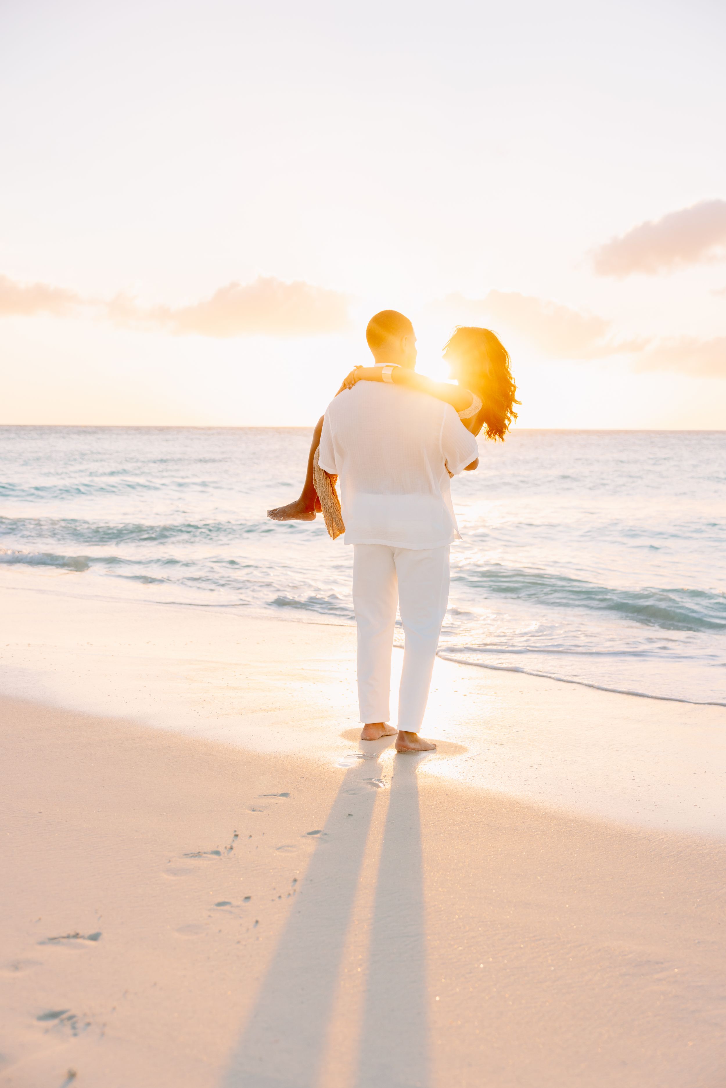 Silhouetted couple walking along beach shoreline during vibrant sunset.