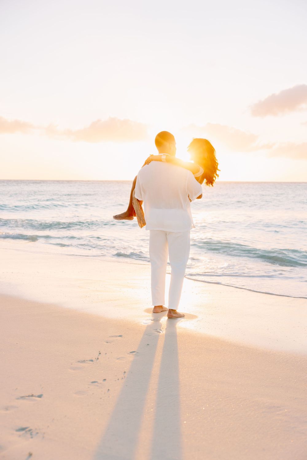Silhouetted couple walking along beach shoreline during vibrant sunset.