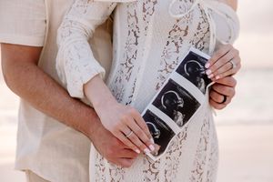 Close-up of hands holding ultrasound photos on lace dress background.