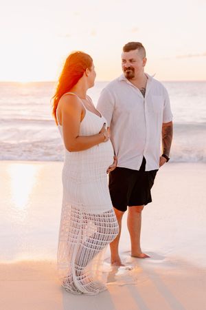 Couple walking along beach shore during golden hour sunset.
