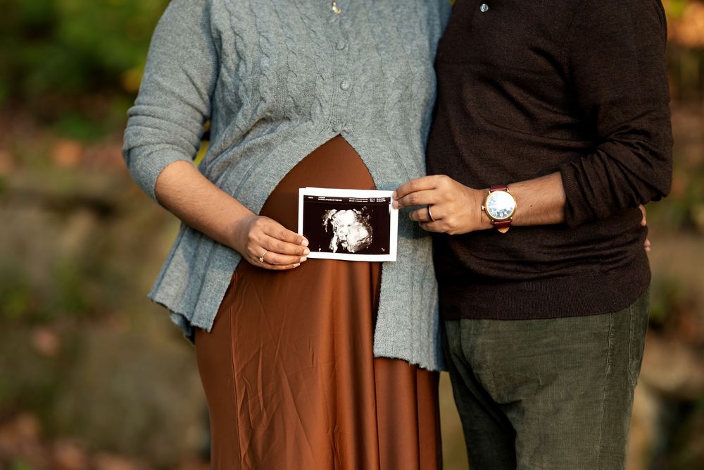 Close-up of expecting couple holding baby ultrasound image together outdoors in autumn park.