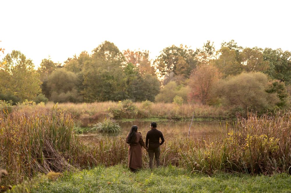 Couple standing together admiring a serene pond landscape with warm autumn colors at golden hour.
