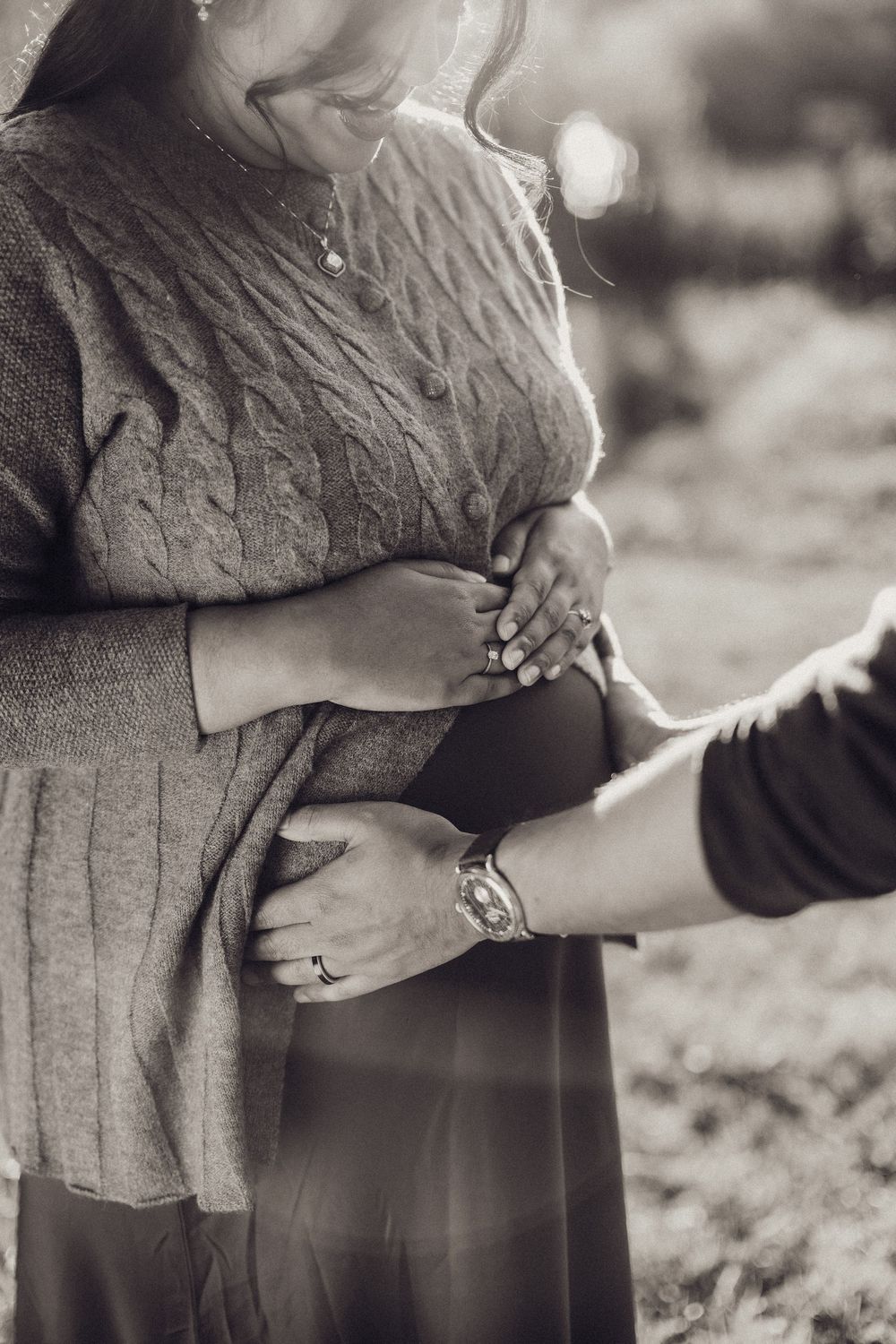 Black and white close-up of pregnant woman's belly with partner's hands gently cradling it.