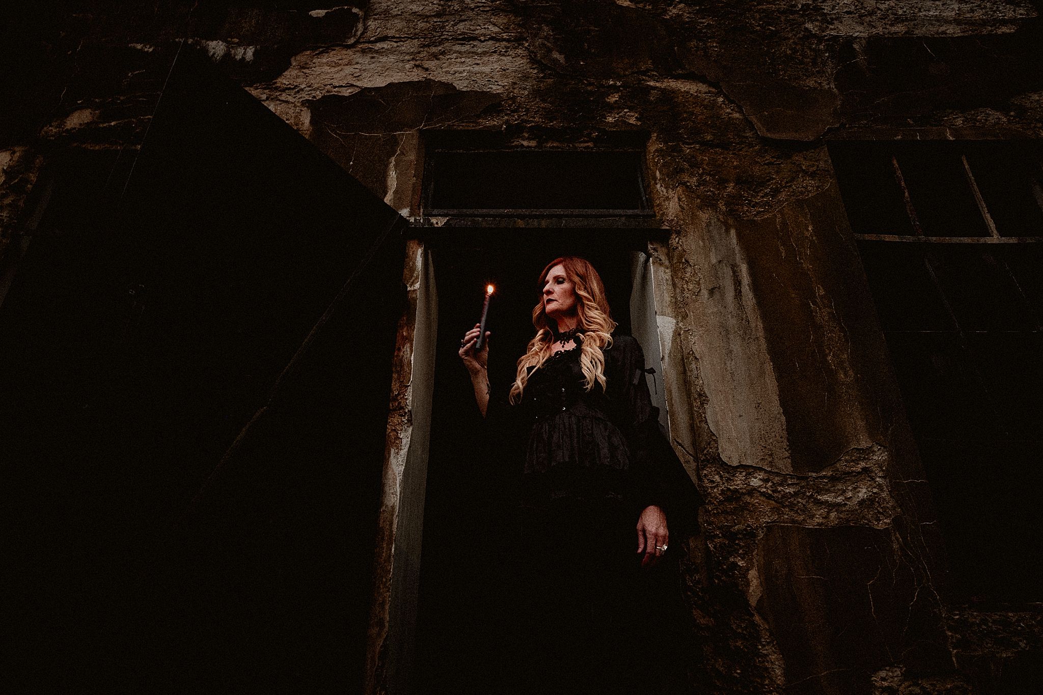 A dark and moody scene of an old stone staircase leading down into a dimly lit underground passage.