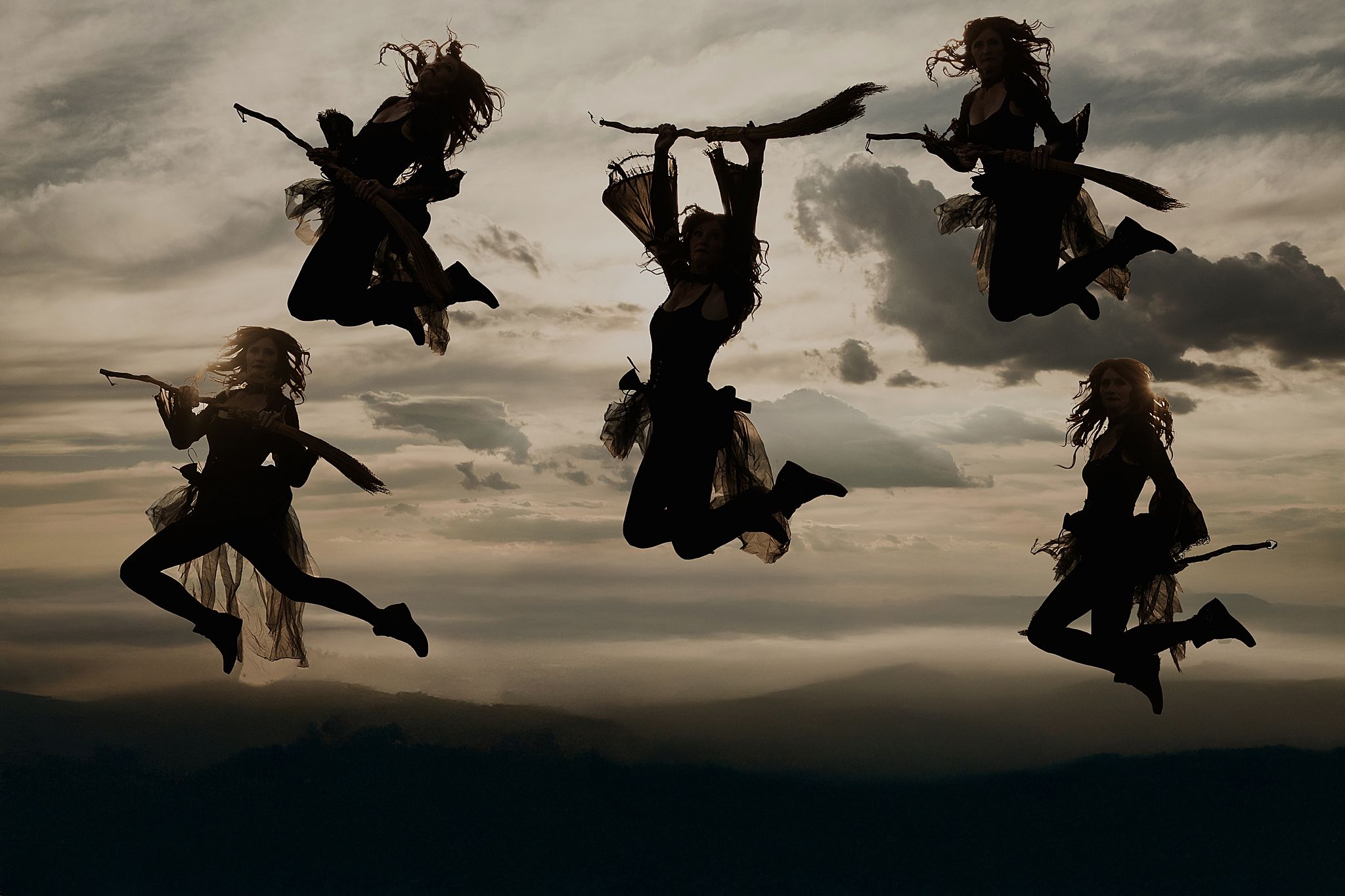 Silhouettes of skydivers performing formations against a dramatic cloudy sunset sky.