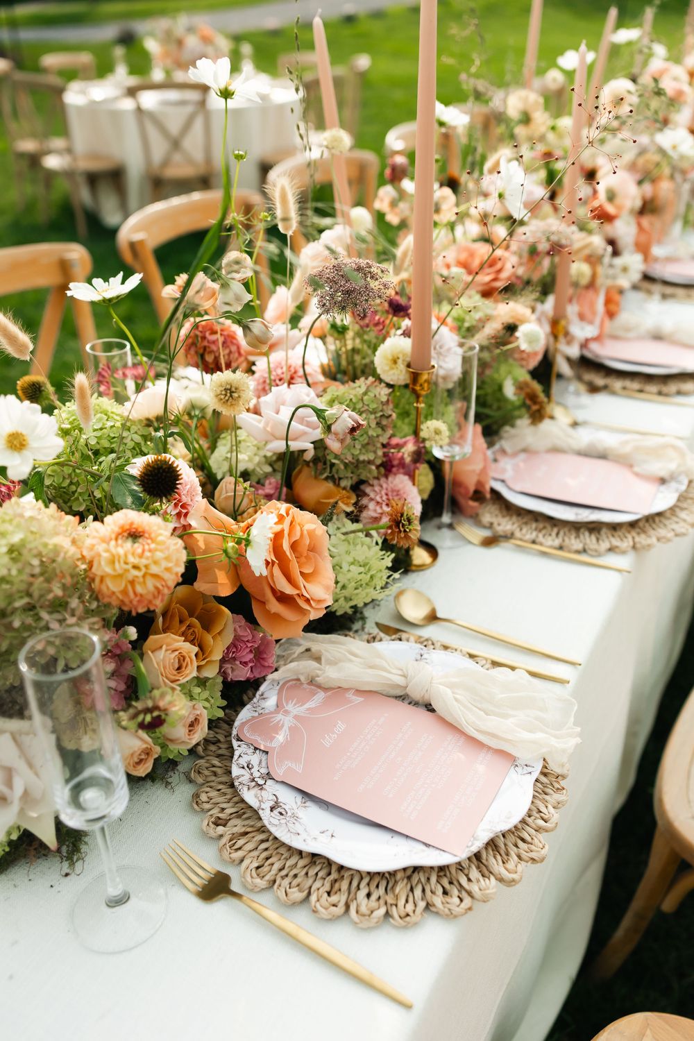 An elegant wedding table setting with pink and peach floral arrangements and gold accents.