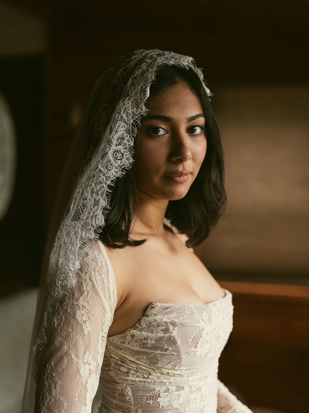A bride wearing a delicate lace wedding dress in a soft, romantic indoor setting.