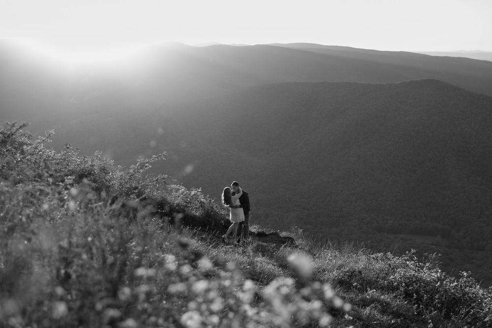 Dramatic black and white landscape photograph of rolling hills and mountains in misty conditions.