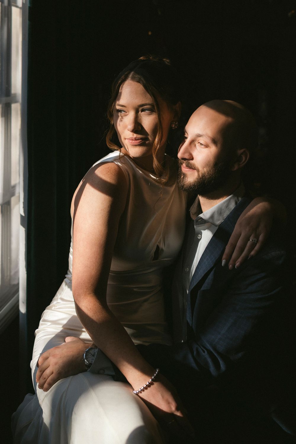 Intimate indoor portrait session with a couple in formal attire sharing tender moments by a window.