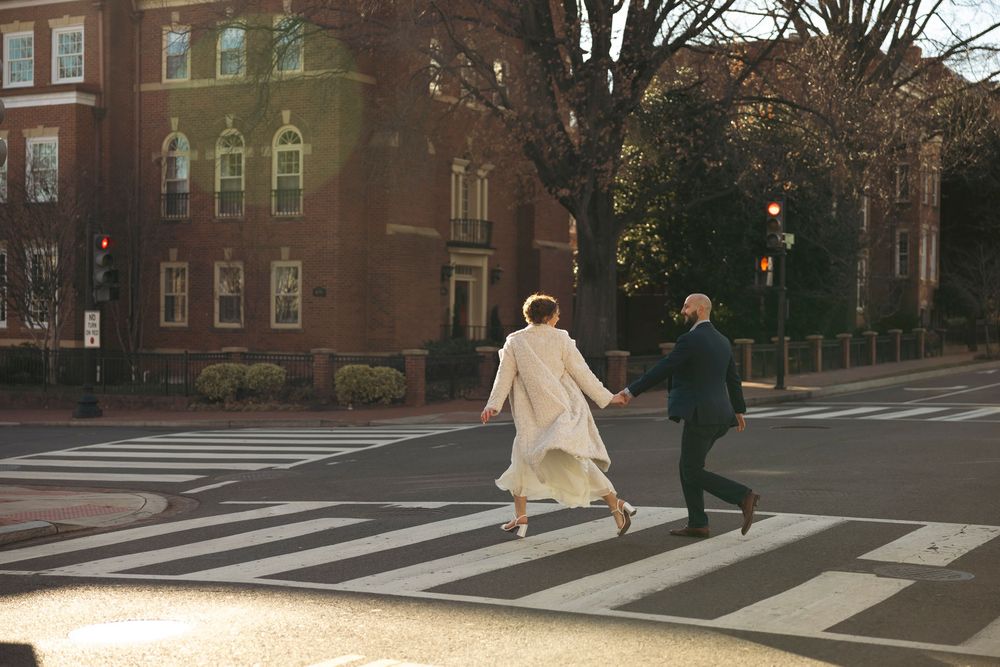 People walking past brick buildings and bare trees on a city sidewalk in winter.