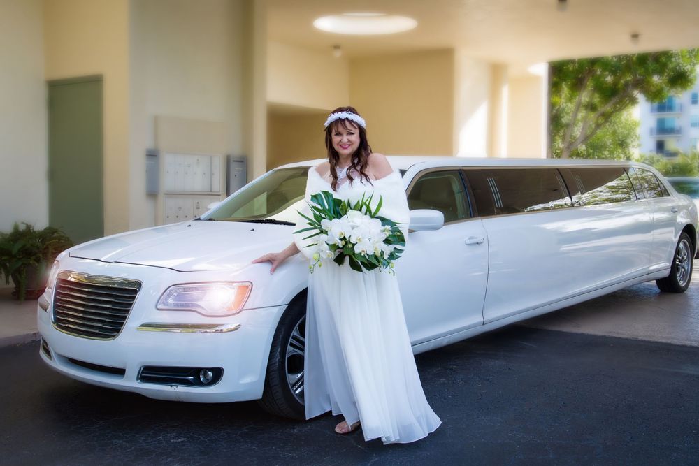 White stretch limousine decorated with floral arrangement parked outside building entrance for wedding celebration.