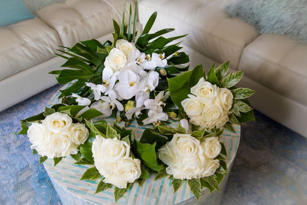 A cascading white rose and orchid bridal bouquet with green foliage arranged on a light blue surface.