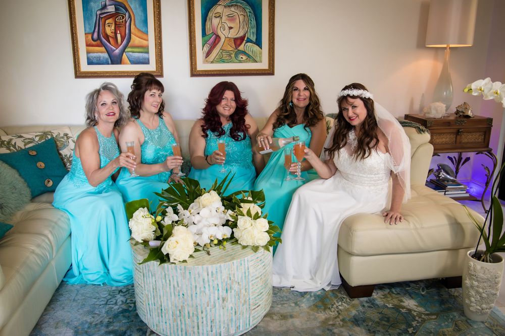 Wedding party members in turquoise dresses gather on a couch with white floral bouquets.