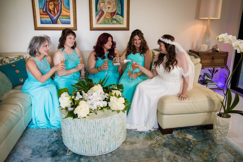 Bridesmaids in matching turquoise dresses sit together on a couch during wedding preparations.