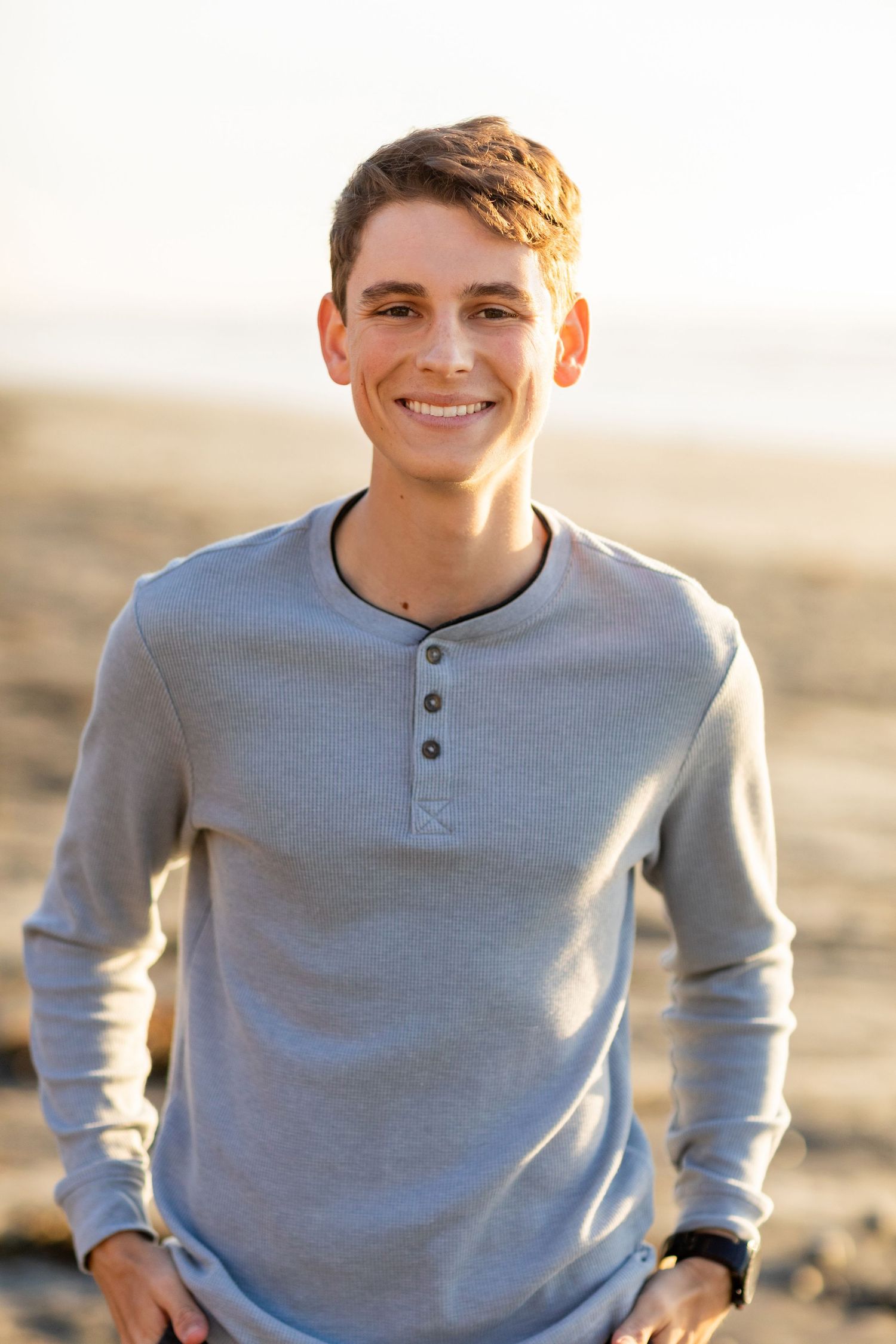 A person wearing a light gray henley shirt smiles while sitting outdoors in warm sunlight.