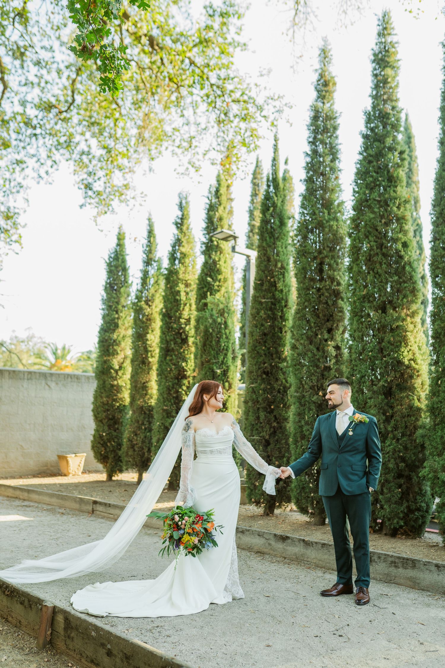 A romantic wedding photoshoot sequence with a couple posing among tall cypress trees in a garden setting.