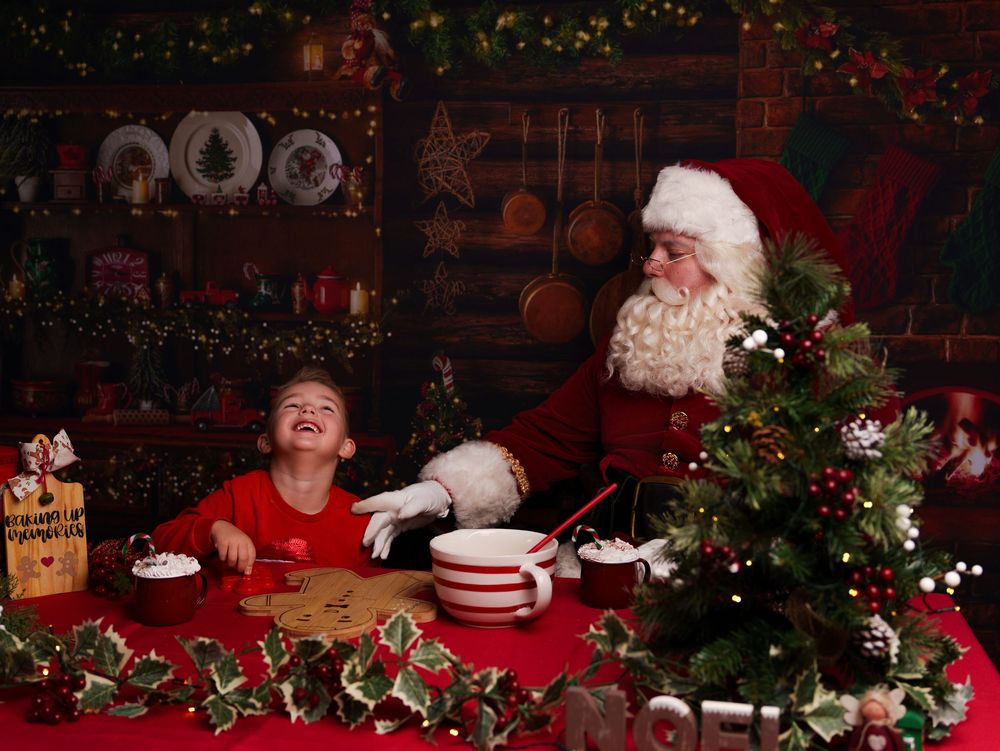 A festive Christmas scene with Santa Claus and a child sharing cookies at a decorated table with holiday decor.