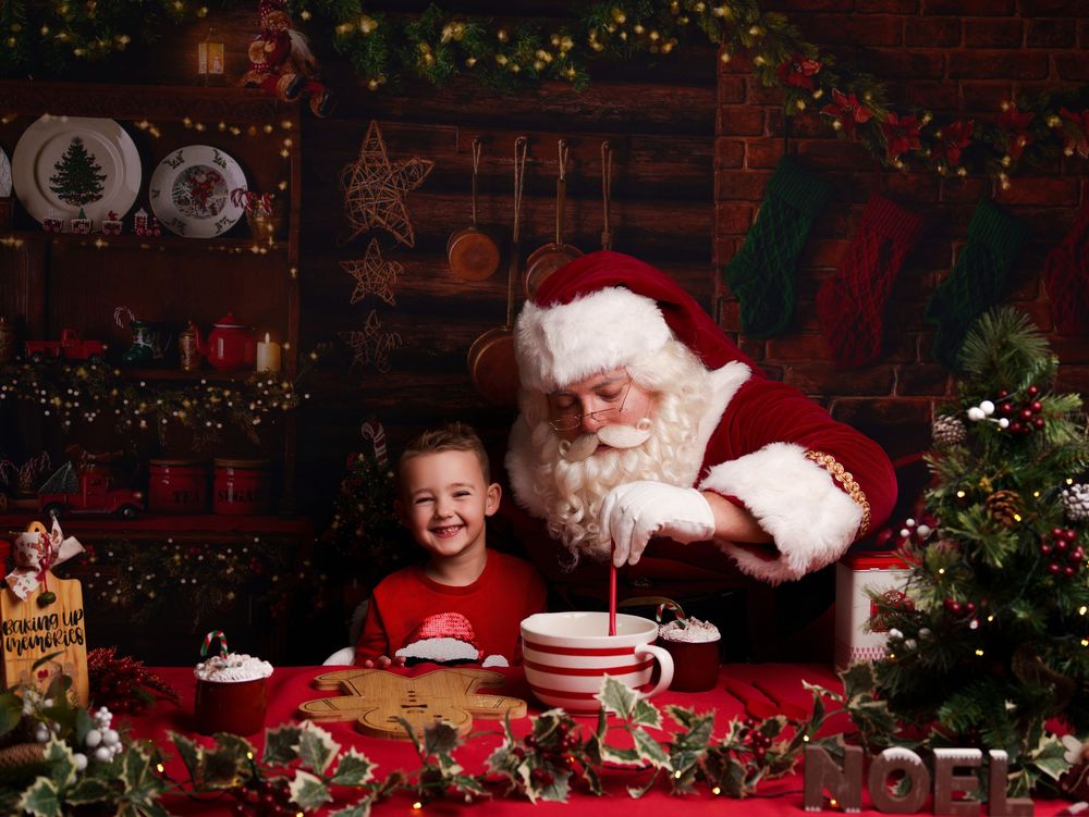 A festive Christmas scene with Santa Claus and a young visitor sharing cookies and hot cocoa at a decorated holiday table.