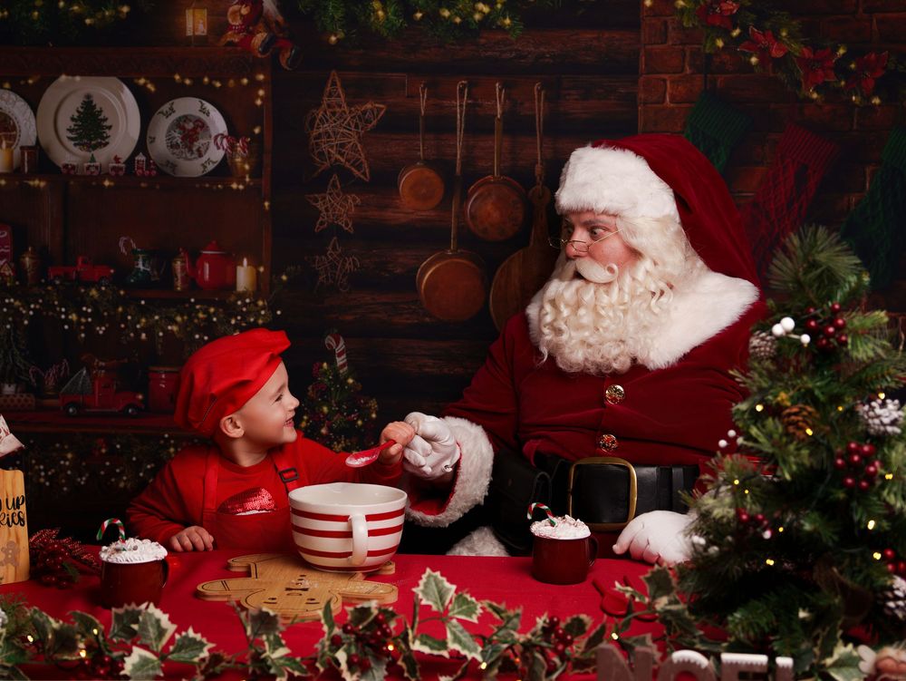 A festive Christmas scene with Santa Claus sharing cookies and hot cocoa amid holiday decorations and twinkling lights.