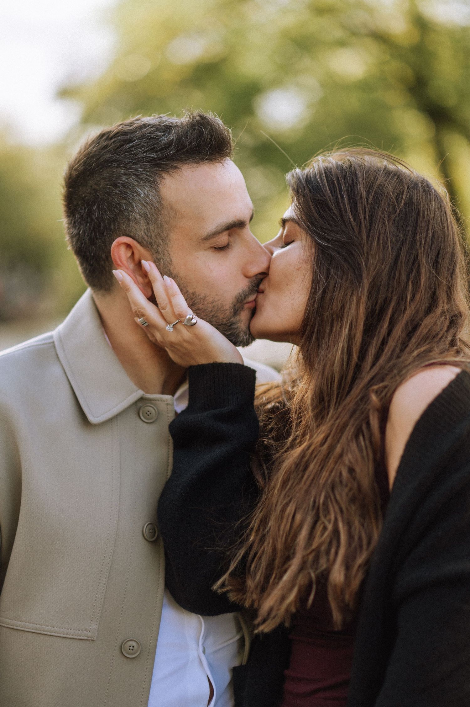 Woman gently touching man’s face during an intimate marriage proposal in Amsterdam, greenery behind.