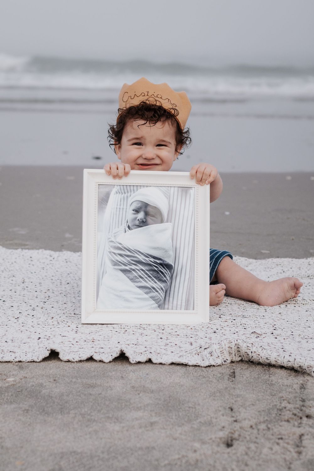 Child lying on beach blanket holds up black and white ultrasound photos.