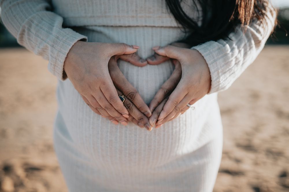 Couple holding hands forming a heart shape on pregnant lady's belly taken by a Melbourne maternity photographer during a sunrise session.