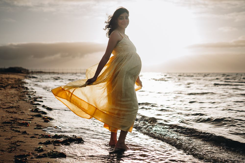 Portrait of a pregnant lady with her yellow flowy dress by the beach during a sunrise Melbourne maternity photo session.