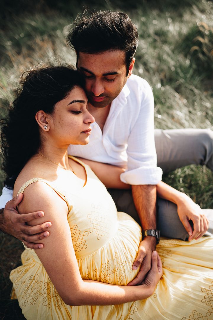 A pregnant couple holding on the belly embracing each other on a grassy field taken by Melbourne maternity photographer.
