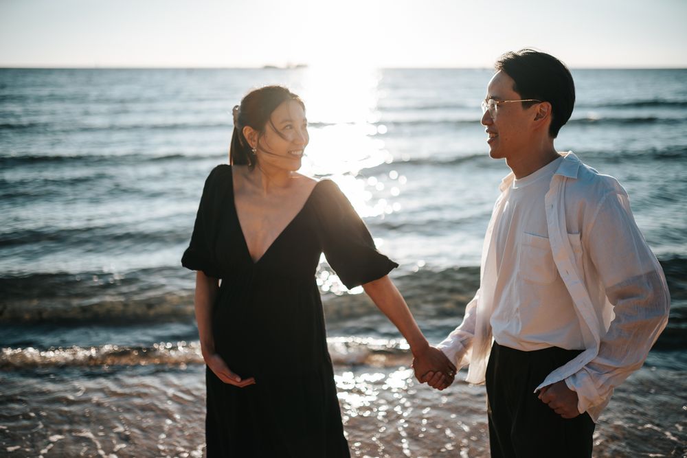 Loving pregnant couple holding hands by the beach during sunset looking cinematic taken by Melbourne maternity photographer.
