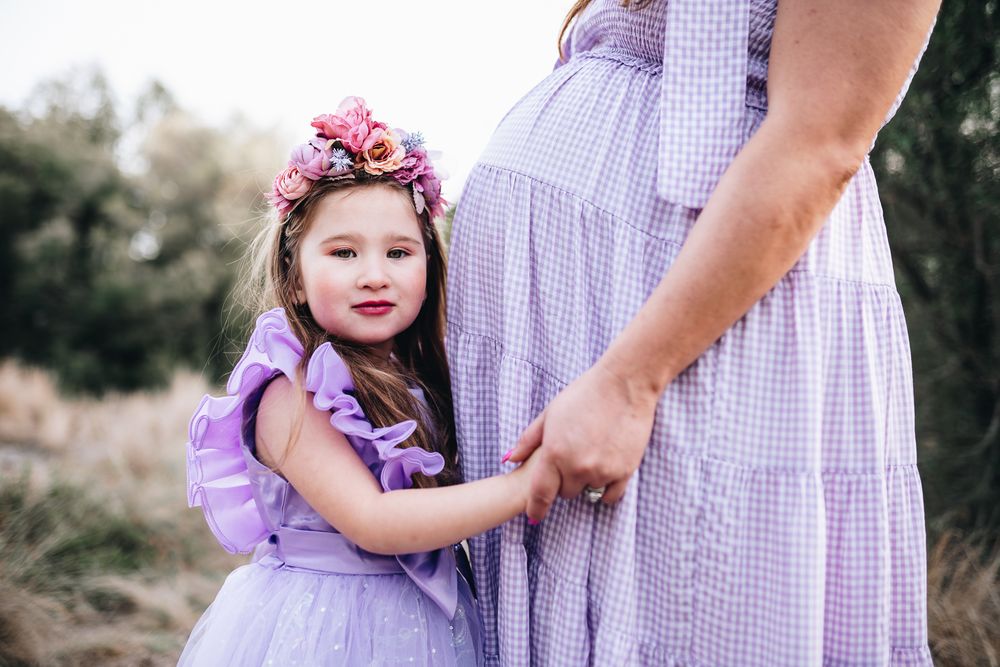 A little girl in purple dress smiling and cuddling mom's pregnant belly taken by a Melbourne maternity photographer.