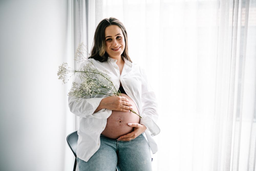 A portrait of a pregnant lady holding a bunch of flowers with soft white backdrop during a Melbourne in home maternity photo session.