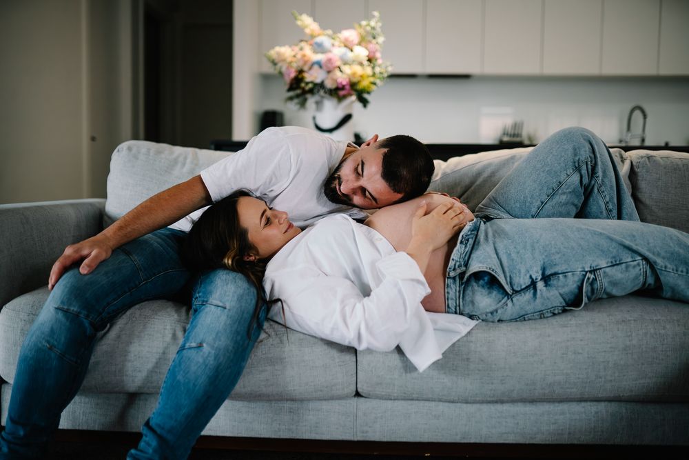A cosy in home maternity session of a pregnant couple lying down on the couch taken by a Melbourne maternity photographer.