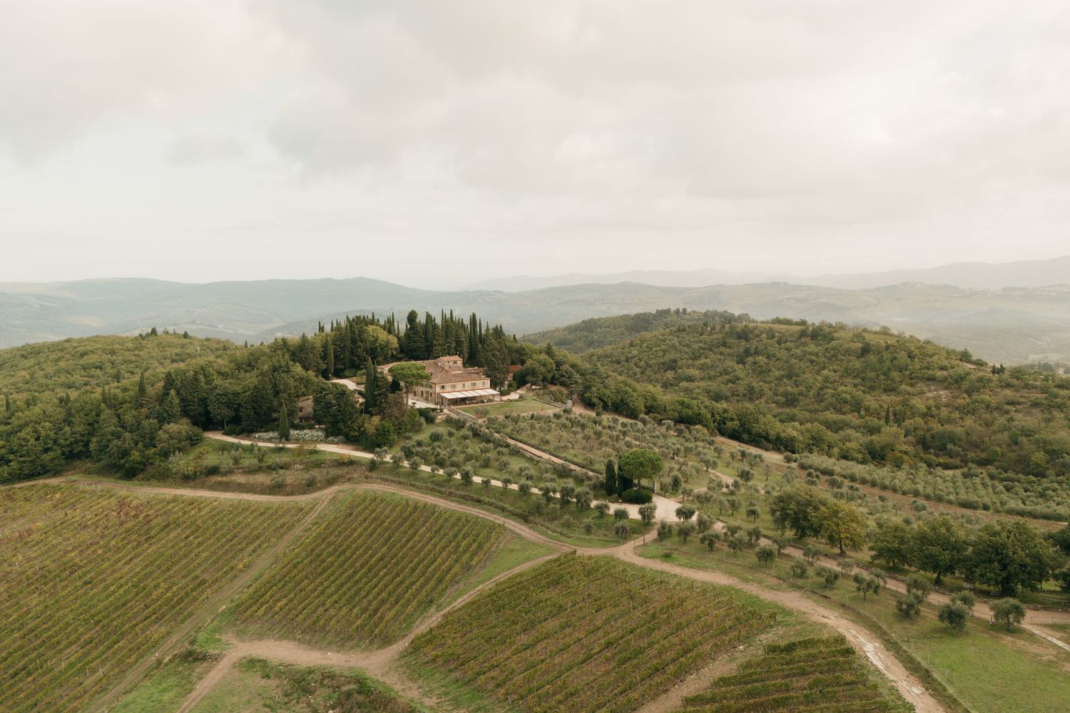 Aerial view of Tuscan villa nestled among rolling hills and vineyards.