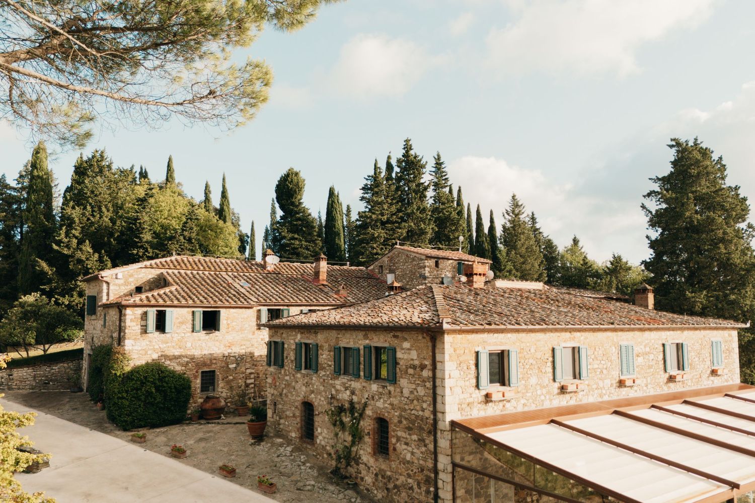 Traditional Italian stone villa with terracotta roof surrounded by cypress trees.