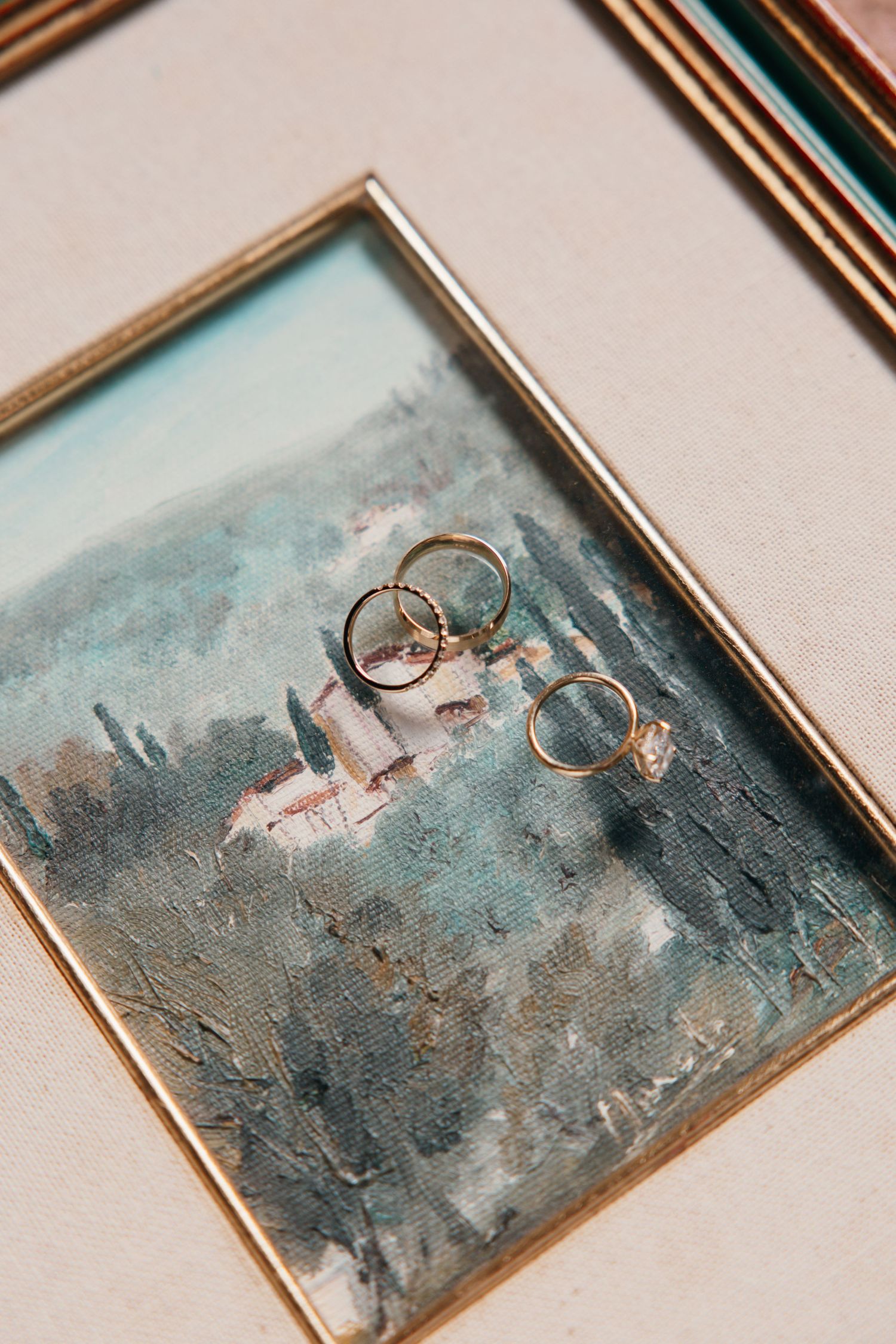 Wedding rings displayed artistically on a blue watercolor background in a gold frame.