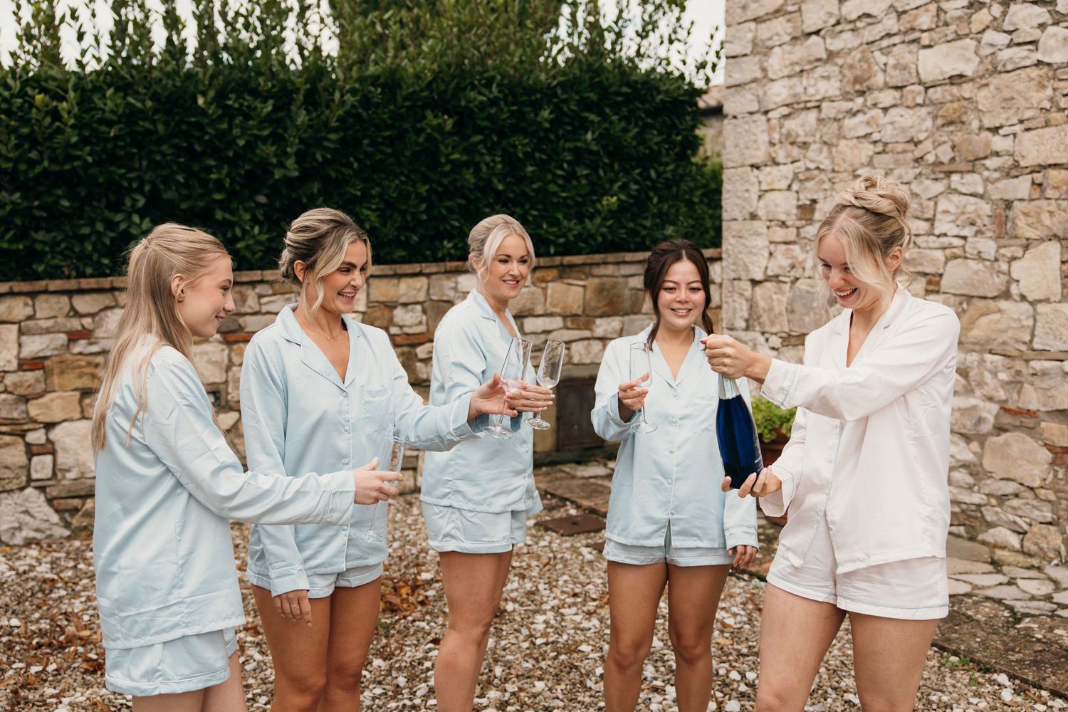 Group of bridesmaids in matching light blue pajama sets standing together outdoors.