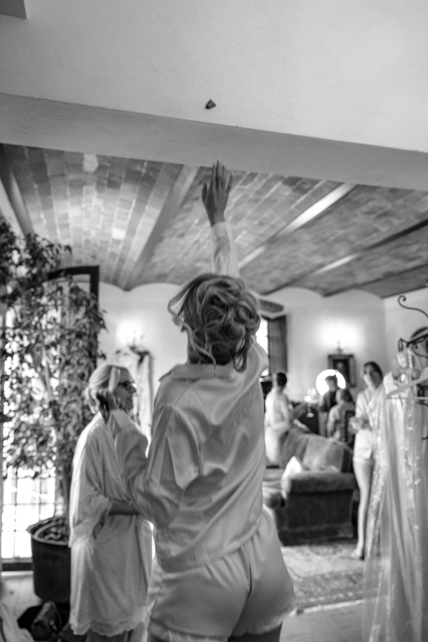 Wedding party in white robes getting ready and celebrating in a rustic room.