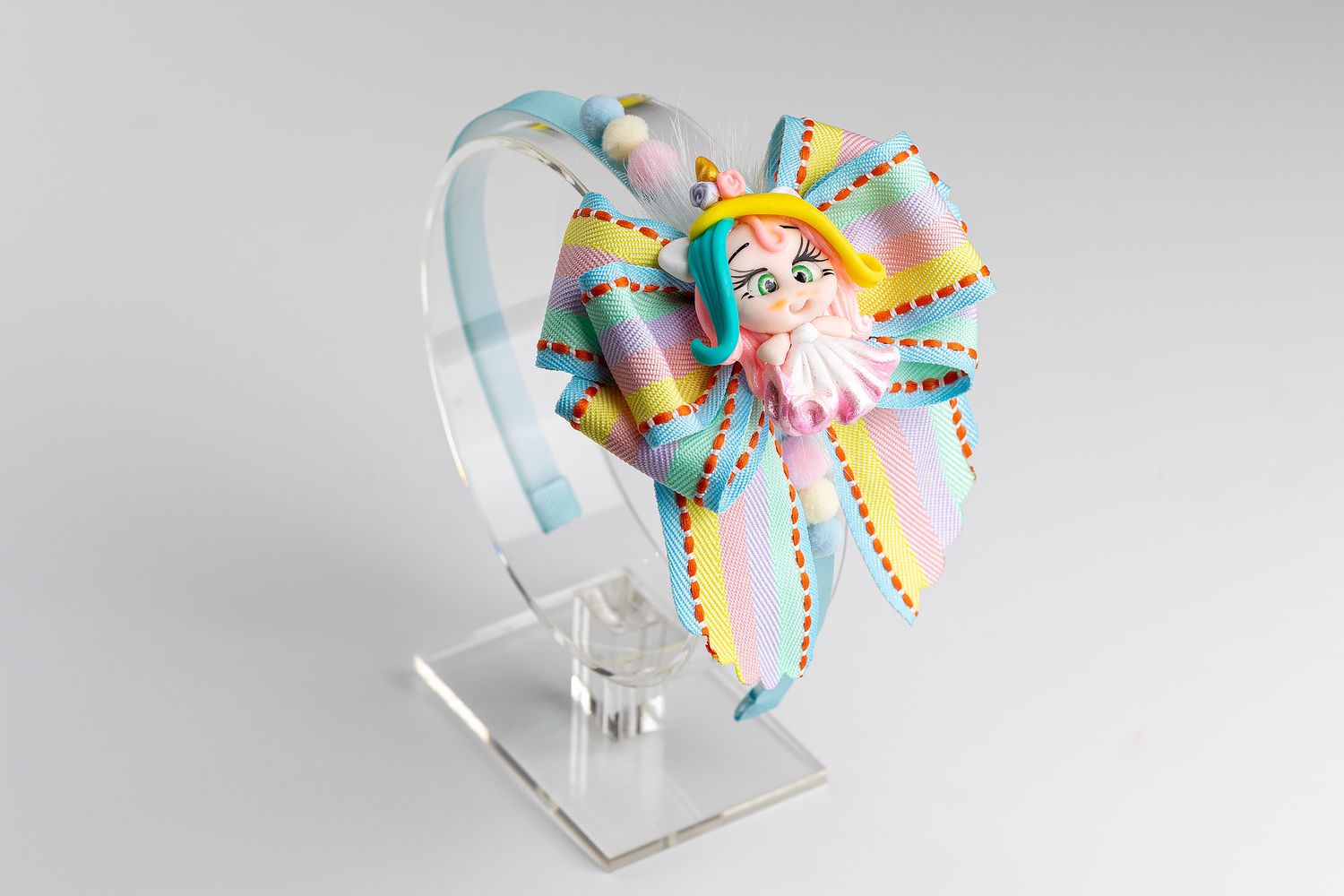 Colorful hair accessory featuring pastel ribbons and decorative elements displayed on a clear plastic stand.