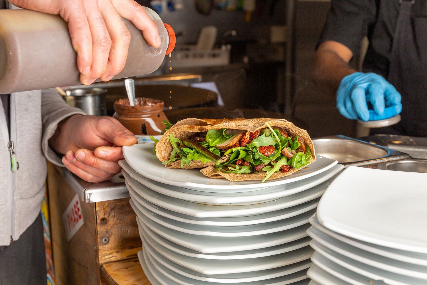 Chef plating a fresh salad on white plates in a restaurant kitchen.