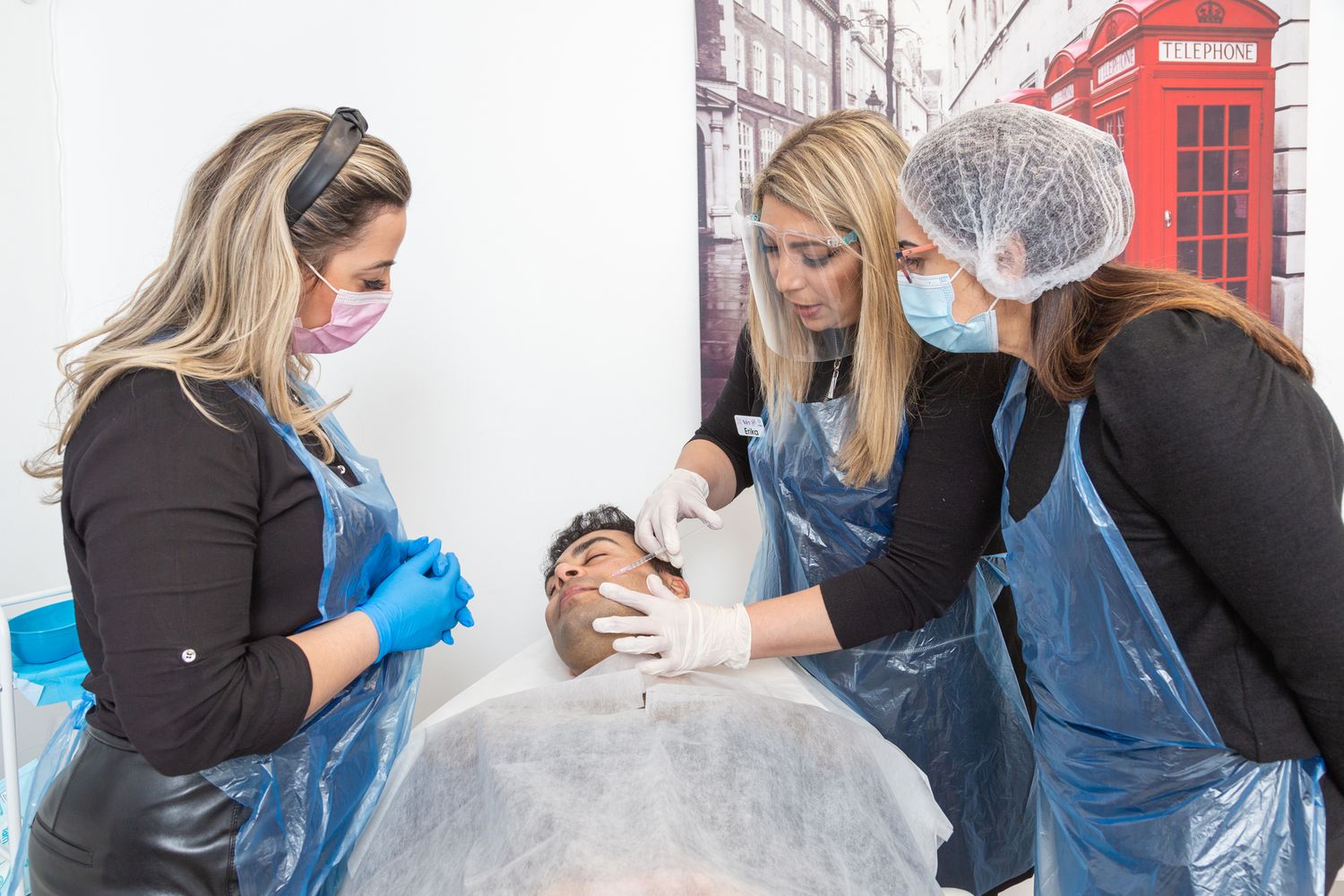Medical professionals in protective gear providing treatment on a table with a London phone booth visible in background.