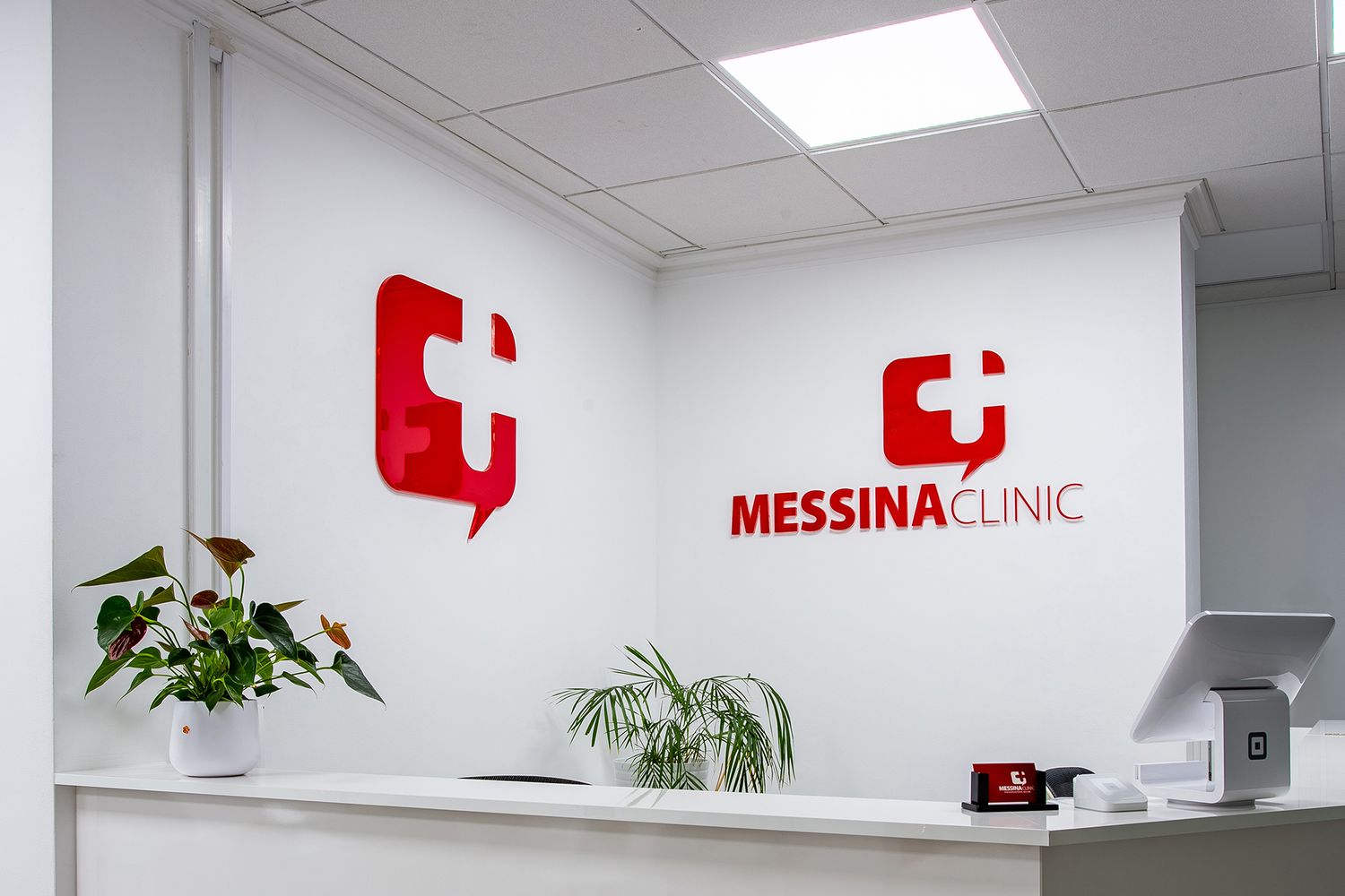 Red Messina Clinic logo and branding displayed on white wall in modern medical office reception area with potted plants.