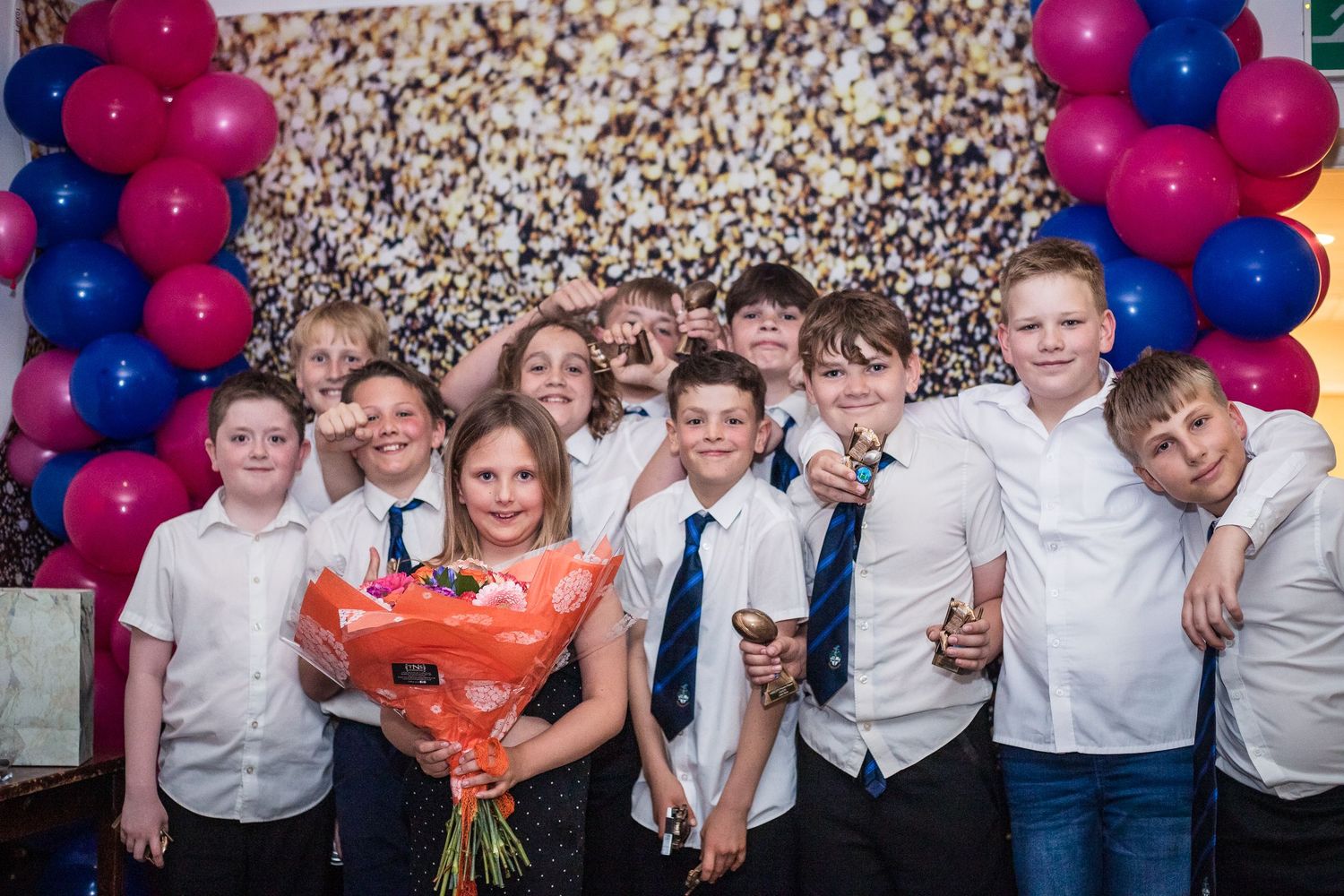 Group of young rugby players wearing white shirts looking at a screen with happy faces at Junior Awards Night