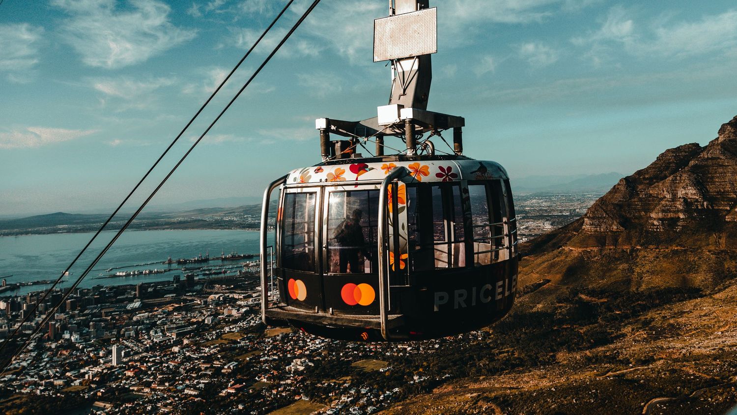 Panoramic view of a coastal city with cable car system and mountains in the distance.
