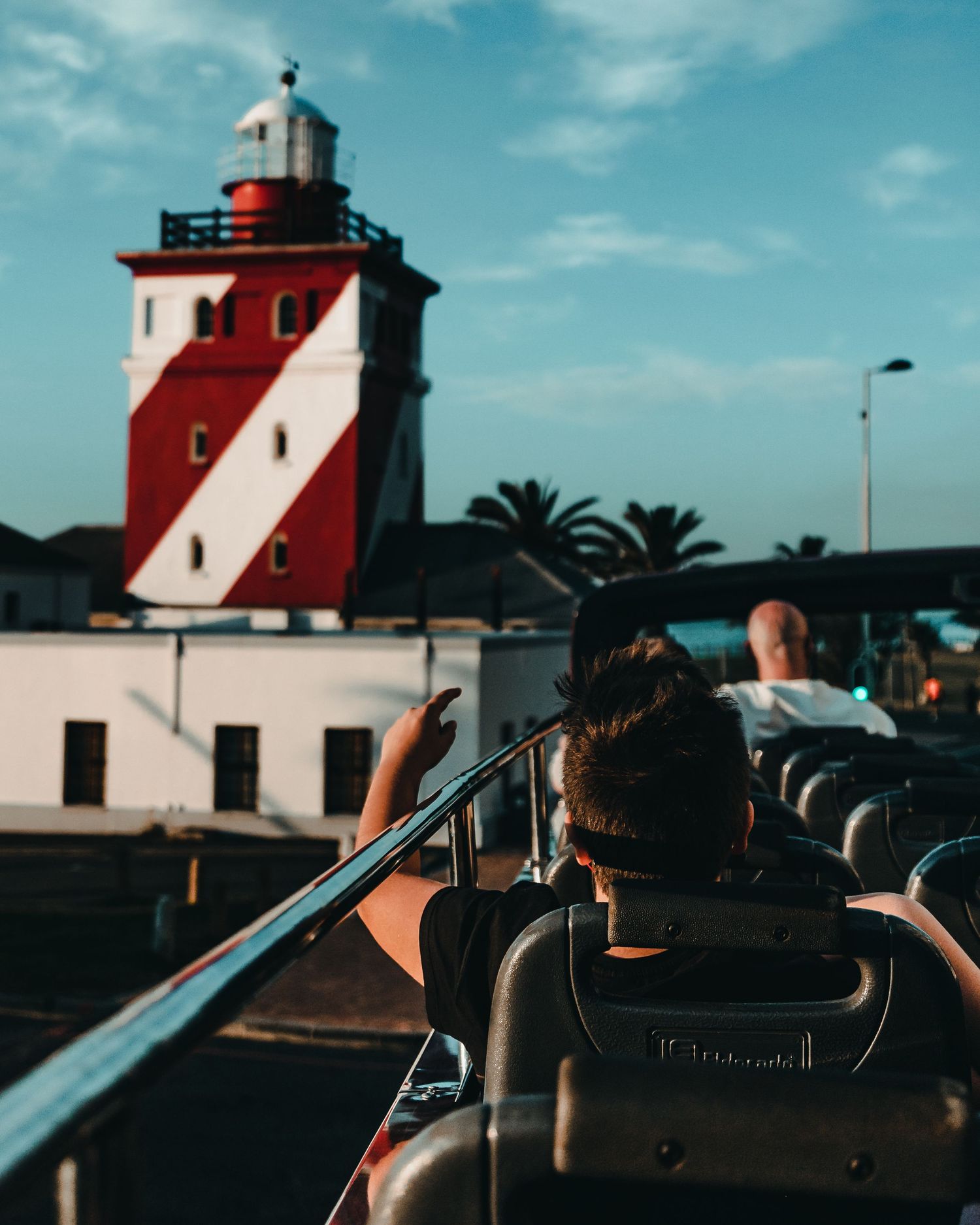 Red and white striped lighthouse stands against bright blue sky with camera equipment in foreground.